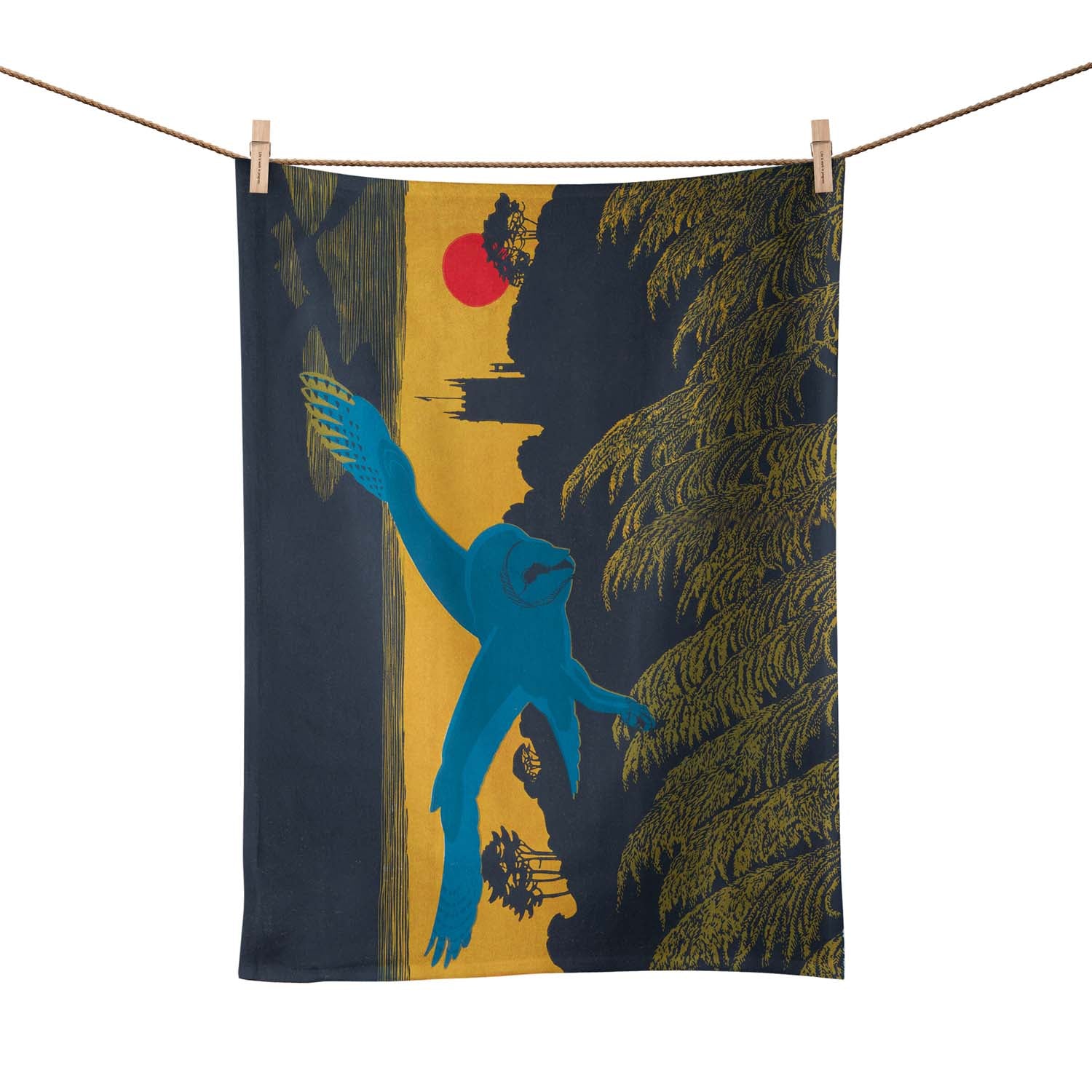 A tea towel pegged on a washing line.  The tea towel shows a blue owl flying over a country scene.