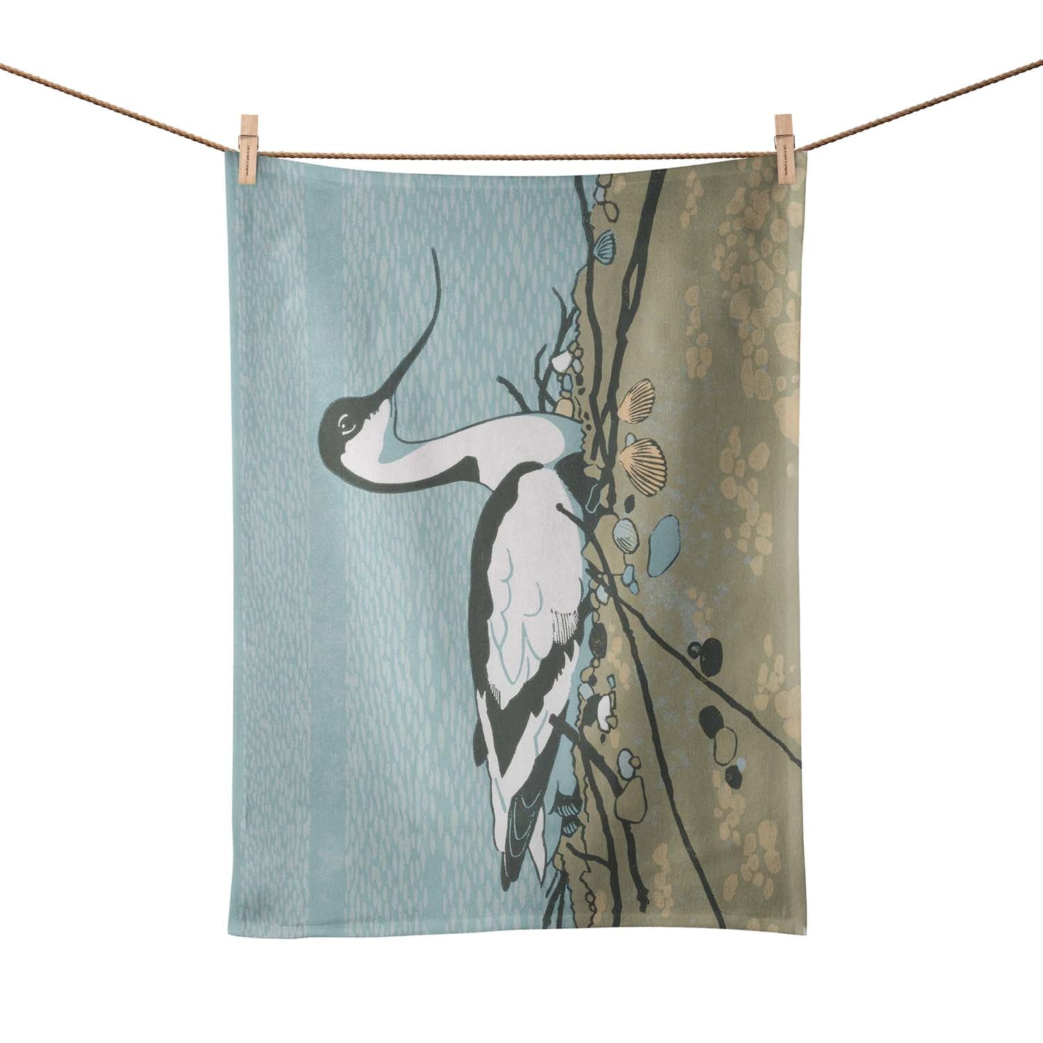 A tea towel pegged on a washing line.  A large avocet is pictured sitting on the sand. 